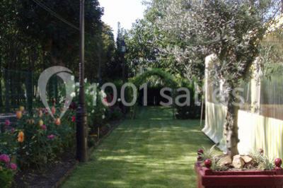 Tente avec table dressée pour un buffet, entourée de chaises blanches, installée sur une pelouse avec haies en arrière-plan.