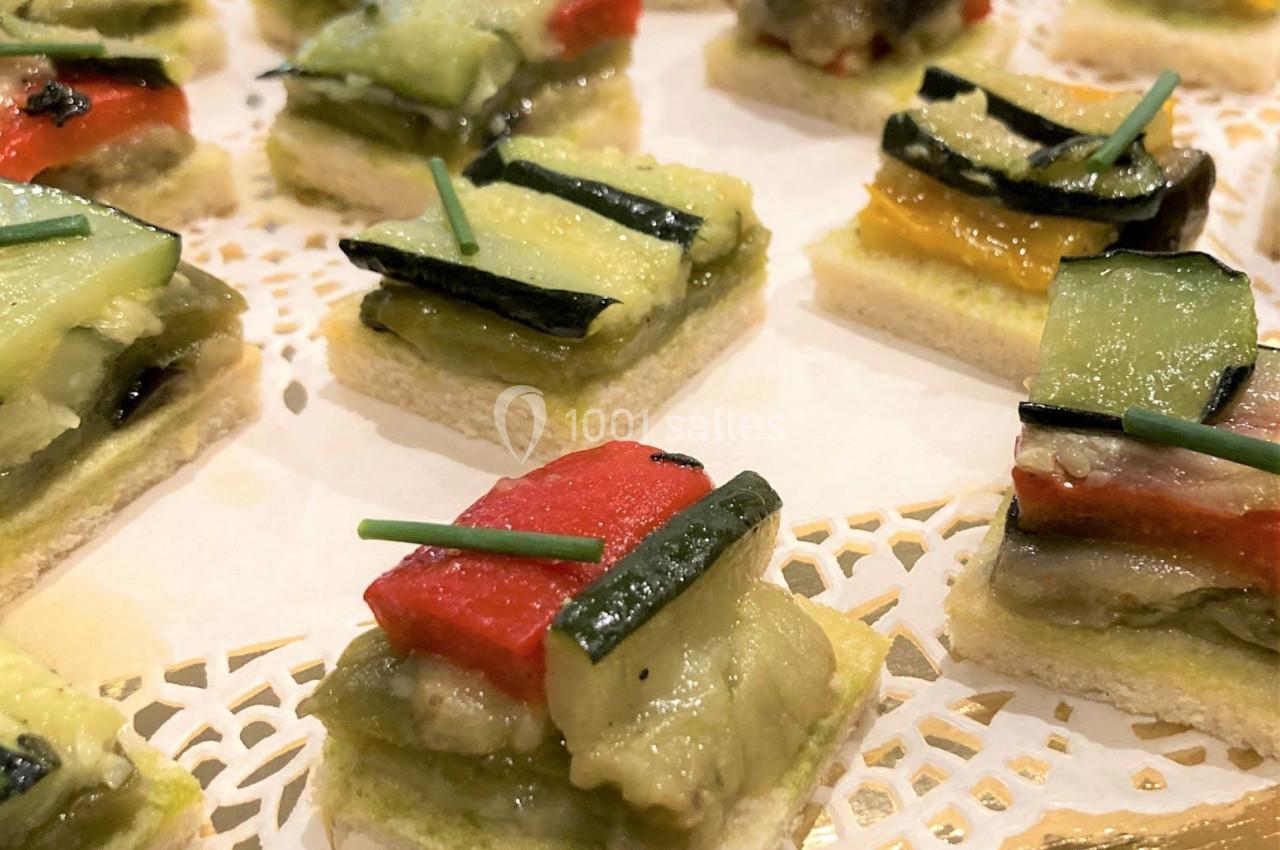 Carrés de pain garnis de légumes grillés colorés, décorés de brins de ciboulette, disposés sur un napperon blanc.