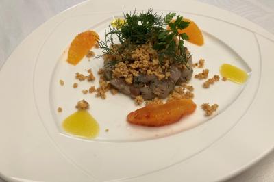 Homme concentré cuisinant en extérieur sur une plancha, entouré de végétation sous un ciel nuageux.