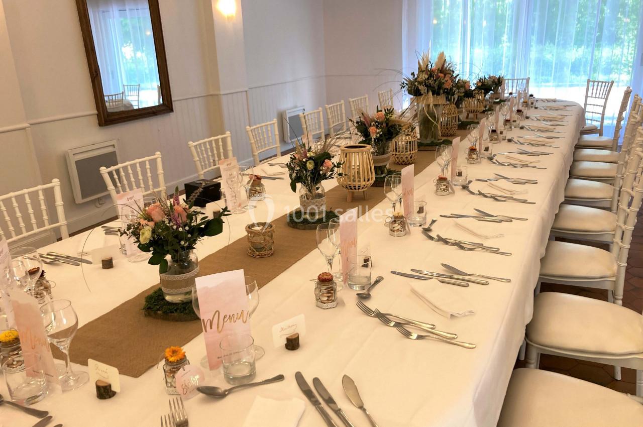 Table dressée pour un repas festif avec nappes blanches, décorations florales et menus disposés sur les assiettes.