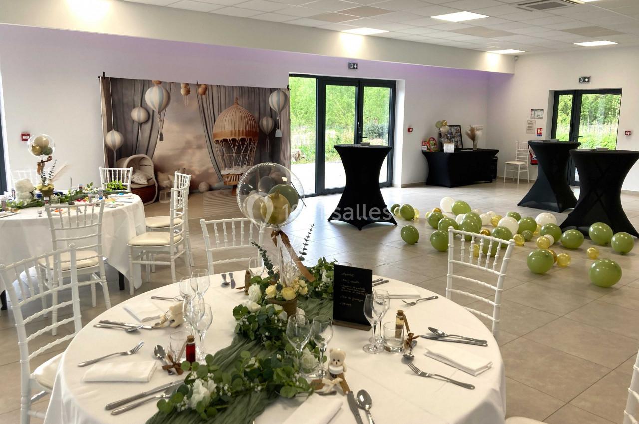 Salle décorée pour un événement avec tables dressées, ballons verts au sol et fond photo avec montgolfière.