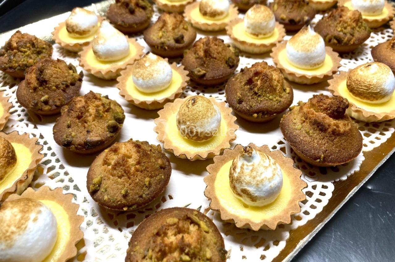 Assortiment de mini-tartelettes garnies de meringue dorée et de petits gâteaux aux éclats de pistache.