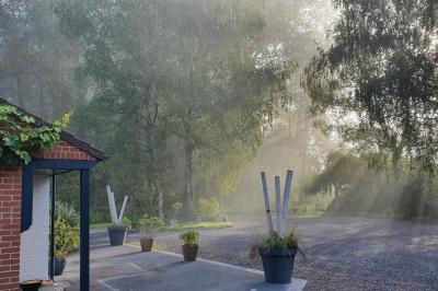 Homme concentré cuisinant en extérieur sur une plancha, entouré de végétation sous un ciel nuageux.