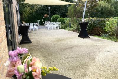 Homme concentré cuisinant en extérieur sur une plancha, entouré de végétation sous un ciel nuageux.