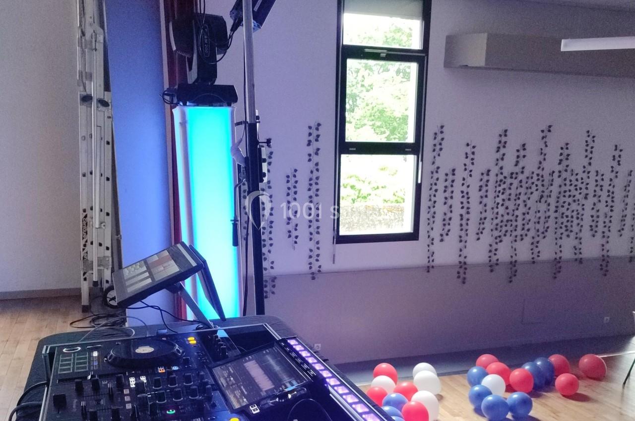 Poste de DJ avec platines et éclairage coloré dans une salle décorée de ballons et motifs muraux, près d'une fenêtre.