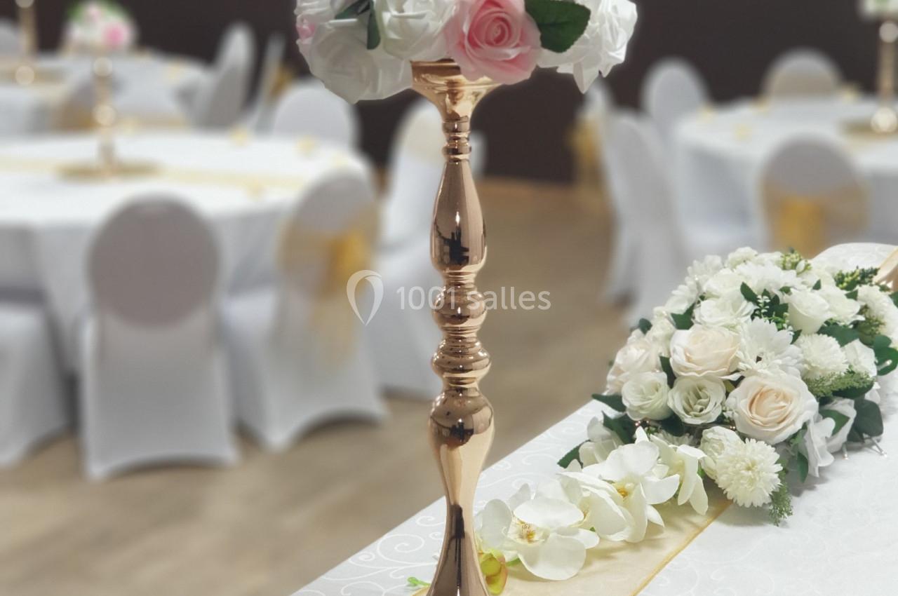 Centre de table en métal doré avec un bouquet de roses blanches et roses, sur une table de réception décorée.