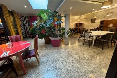Salle de restaurant chaleureuse avec tables en bois, chaises assorties, luminaires suspendus et plantes décoratives.