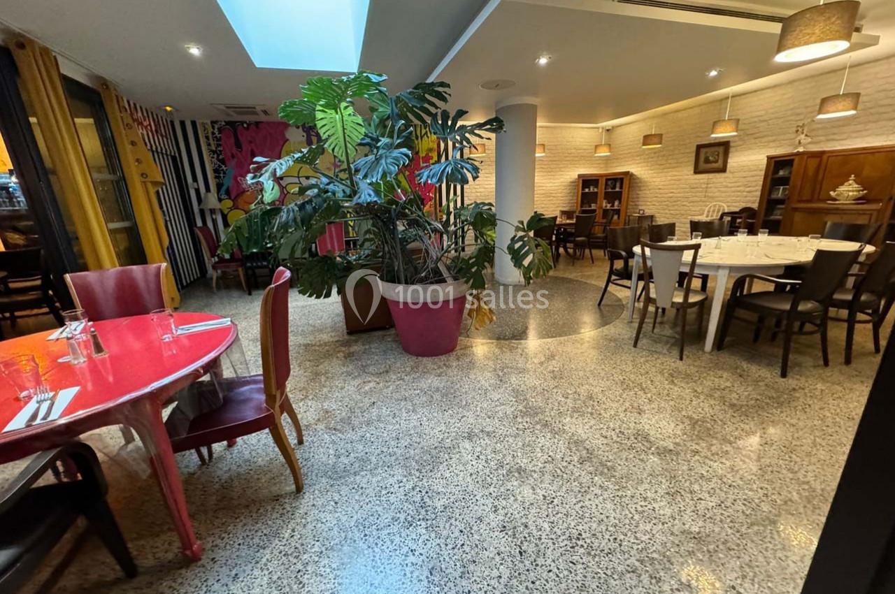 Salle de restaurant lumineuse avec tables dressées, grandes plantes en pot et décoration murale colorée.