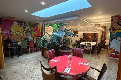Salle de restaurant chaleureuse avec tables en bois, chaises assorties, luminaires suspendus et plantes décoratives.