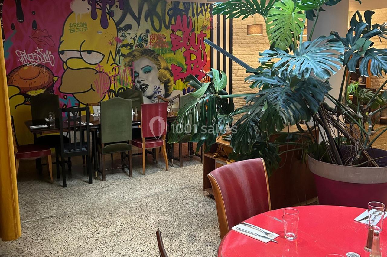 Salle de restaurant colorée avec des graffitis sur les murs, des plantes vertes et des tables dressées.