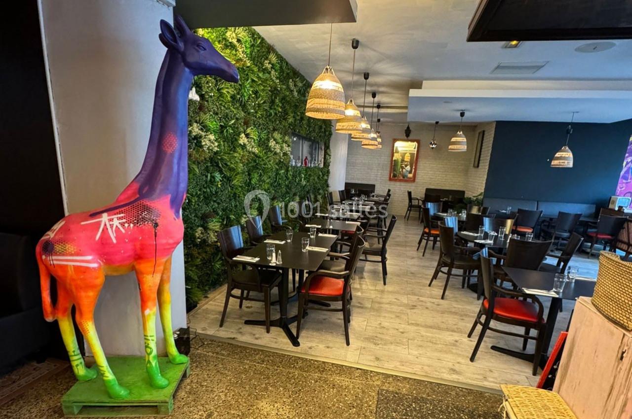 Statue colorée de girafe dans un restaurant moderne avec murs végétalisés et tables dressées.