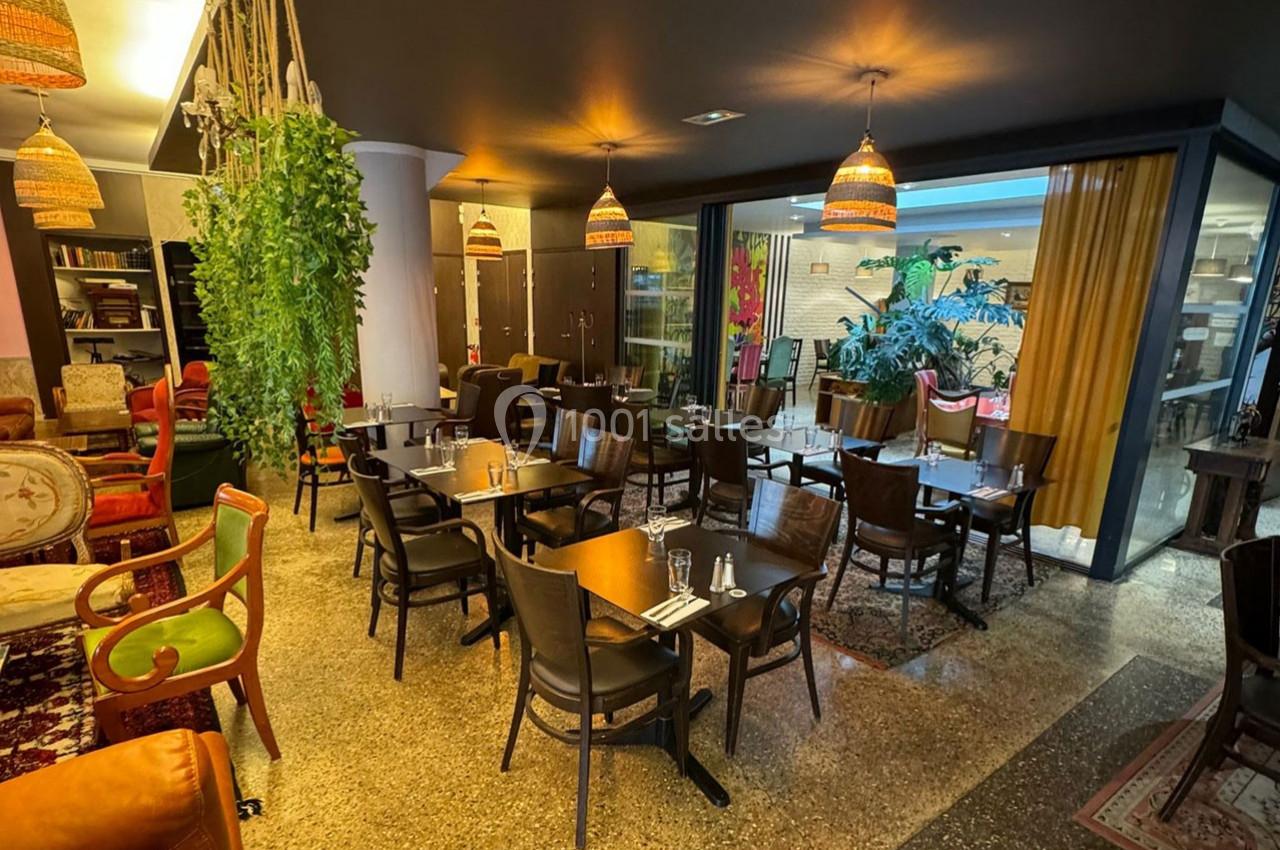 Salle de restaurant chaleureuse avec tables en bois, chaises assorties, luminaires suspendus et plantes décoratives.