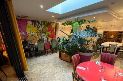 Terrasse d'un café avec des tables et des chaises colorées devant une façade vitrée portant l'inscription ’Au Bout du Bar’.