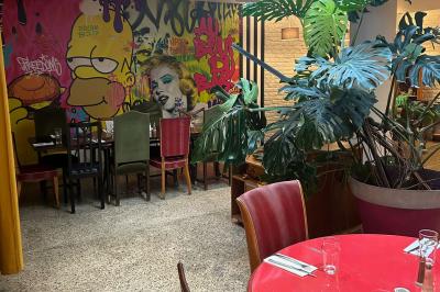 Terrasse d'un café avec des tables et des chaises colorées devant une façade vitrée portant l'inscription ’Au Bout du Bar’.