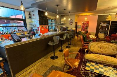 Terrasse d'un café avec des tables et des chaises colorées devant une façade vitrée portant l'inscription ’Au Bout du Bar’.