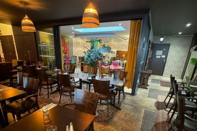 Terrasse d'un café avec des tables et des chaises colorées devant une façade vitrée portant l'inscription ’Au Bout du Bar’.