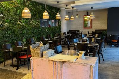 Terrasse d'un café avec des tables et des chaises colorées devant une façade vitrée portant l'inscription ’Au Bout du Bar’.