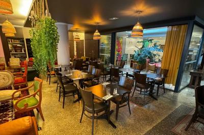 Terrasse d'un café avec des tables et des chaises colorées devant une façade vitrée portant l'inscription ’Au Bout du Bar’.