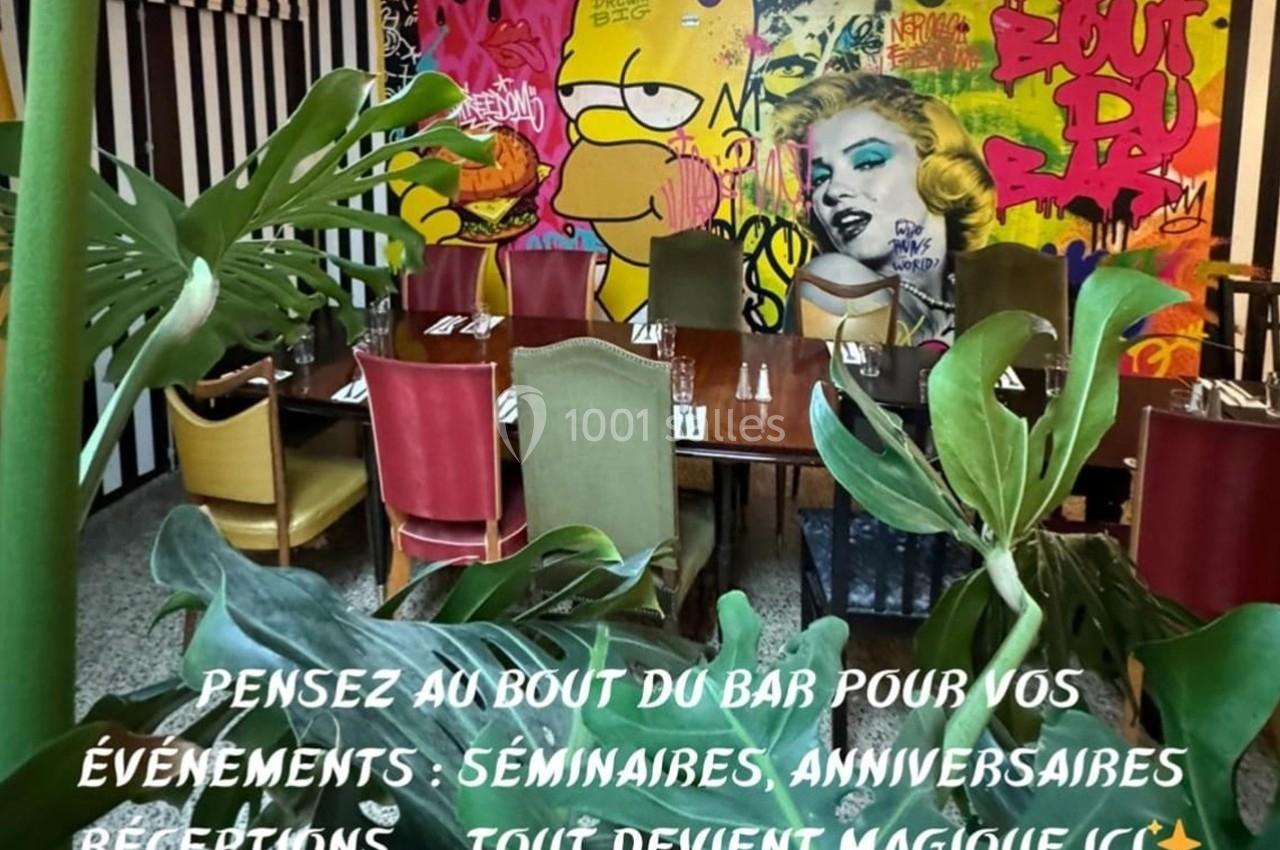 Salle colorée avec des tables dressées, entourée de plantes et décorée d'une fresque murale vive et artistique.