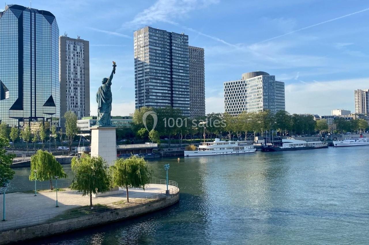 Vue d'une réplique de la Statue de la Liberté à Paris, située sur une île de la Seine, entourée de bâtiments modernes.
