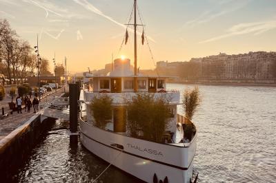Salle de restaurant lumineuse avec des tables dressées, des chaises modernes et vue sur une rivière bordée de bâtiments.