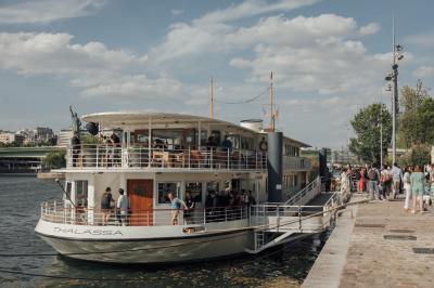 Salle de restaurant lumineuse avec des tables dressées, des chaises modernes et vue sur une rivière bordée de bâtiments.