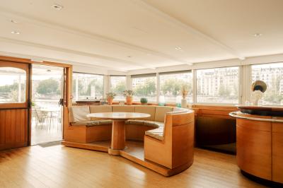 Salle de restaurant lumineuse avec des tables dressées, des chaises modernes et vue sur une rivière bordée de bâtiments.