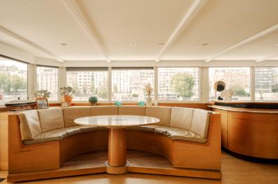 Salle de restaurant lumineuse avec des tables dressées, des chaises modernes et vue sur une rivière bordée de bâtiments.