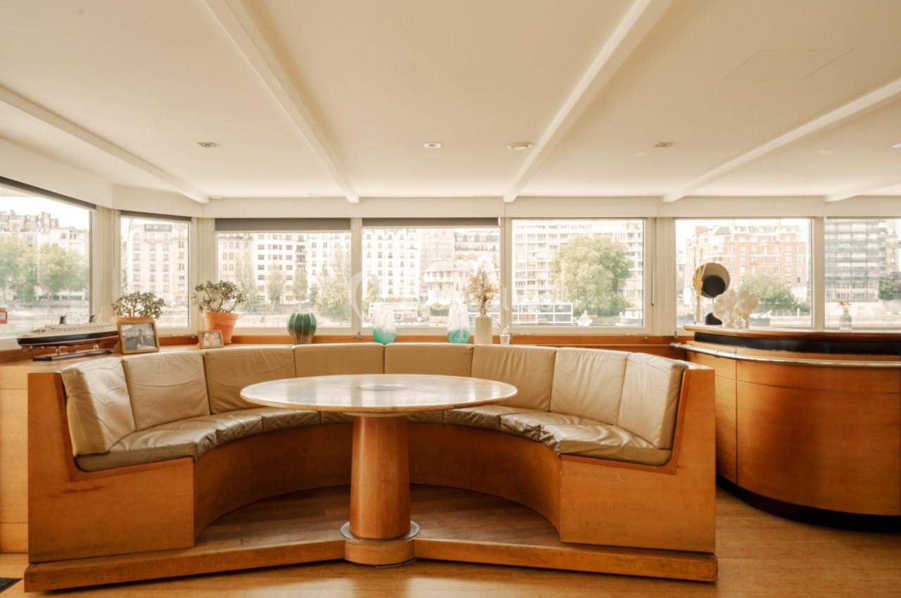 Banquette en cuir beige autour d'une table ronde en bois, située dans une pièce lumineuse avec vue sur des bâtiments.