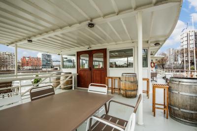 Salle de restaurant lumineuse avec des tables dressées, des chaises modernes et vue sur une rivière bordée de bâtiments.
