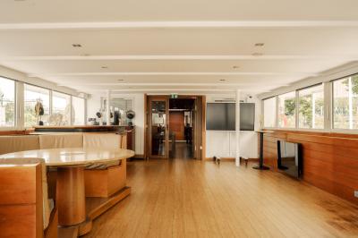 Salle de restaurant lumineuse avec des tables dressées, des chaises modernes et vue sur une rivière bordée de bâtiments.