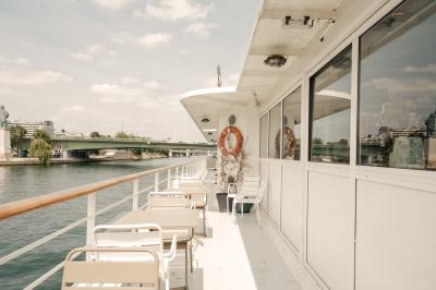 Salle de restaurant lumineuse avec des tables dressées, des chaises modernes et vue sur une rivière bordée de bâtiments.