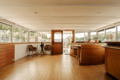 Salle de restaurant lumineuse avec des tables dressées, des chaises modernes et vue sur une rivière bordée de bâtiments.