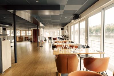 Salle de restaurant lumineuse avec des tables dressées, des chaises modernes et vue sur une rivière bordée de bâtiments.