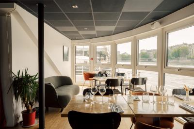 Salle de restaurant lumineuse avec des tables dressées, des chaises modernes et vue sur une rivière bordée de bâtiments.