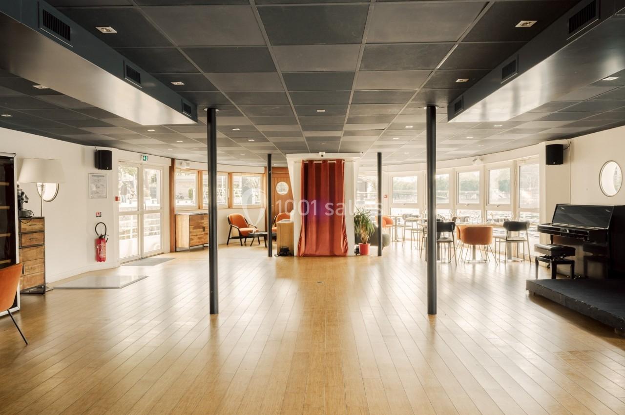 Salle lumineuse avec parquet en bois, grandes fenêtres, mobilier moderne et rideau rouge au centre.