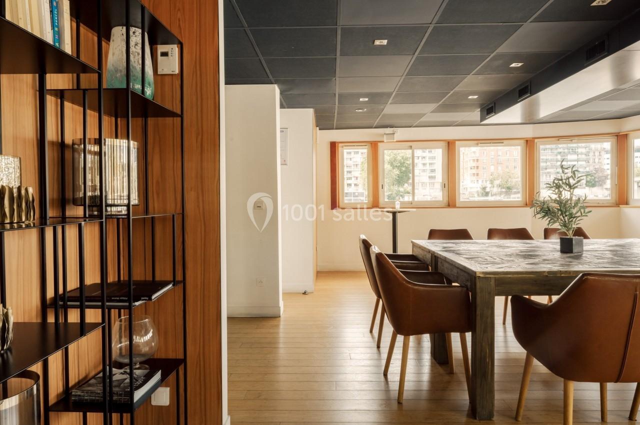 Salle de réunion lumineuse avec table en bois, chaises en cuir et étagère décorative sur un sol en parquet.