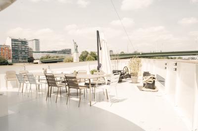 Salle de restaurant lumineuse avec des tables dressées, des chaises modernes et vue sur une rivière bordée de bâtiments.