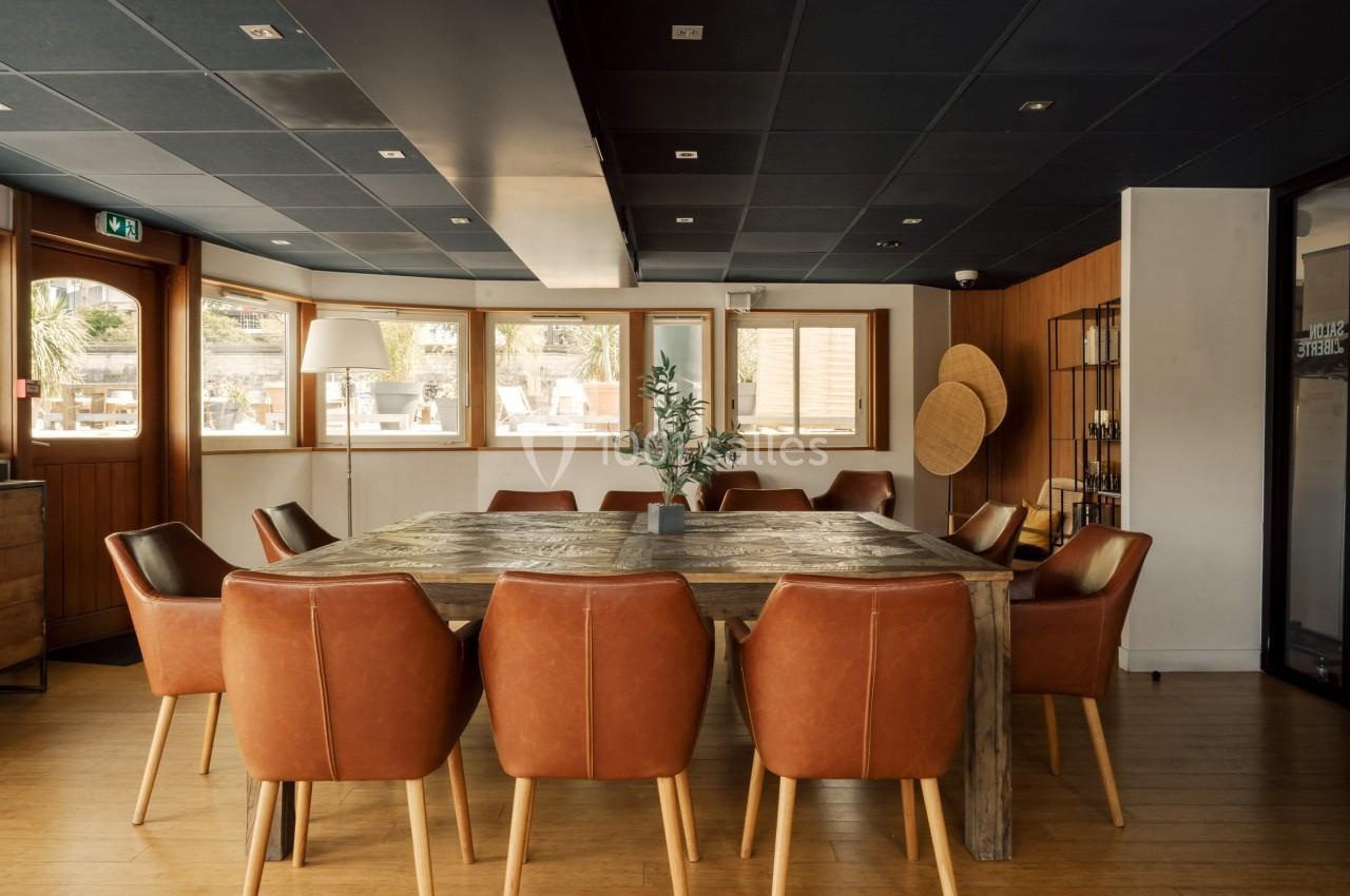 Salle de réunion lumineuse avec table en bois massif, chaises en cuir marron et décoration minimaliste.