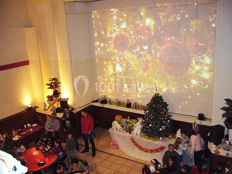 Salle décorée pour Noël avec un sapin, une table festive et une projection lumineuse d'ornements sur un mur.