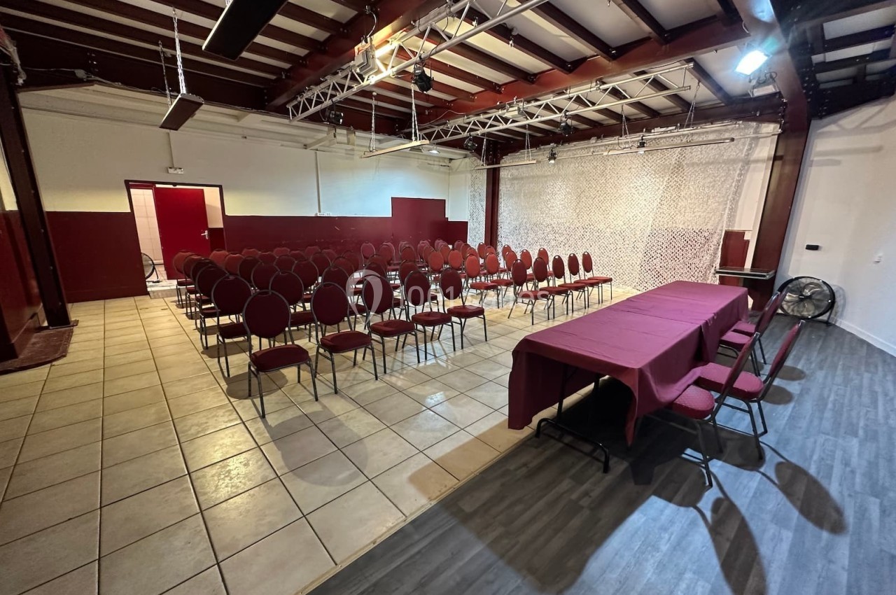 Salle de conférence avec rangées de chaises rouges alignées face à une table recouverte d'une nappe bordeaux.