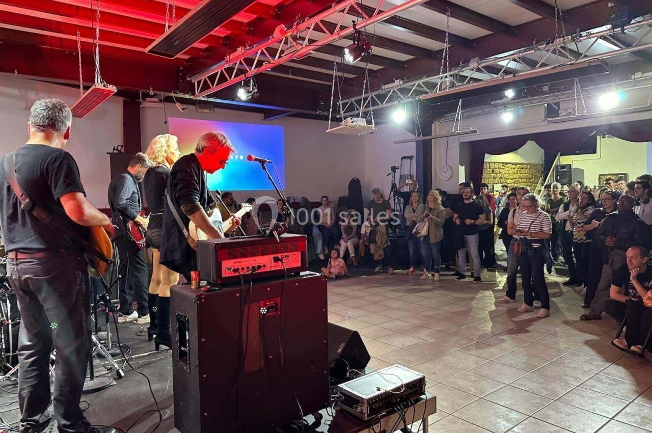 Un groupe de musiciens joue sur scène dans une salle, devant un public debout et attentif.