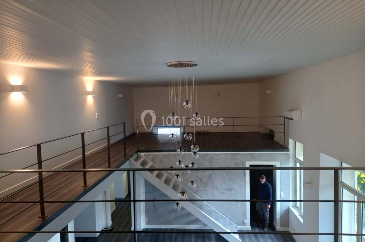 Vue intérieure d'un espace moderne à deux niveaux avec mezzanine, escalier central et éclairage suspendu.