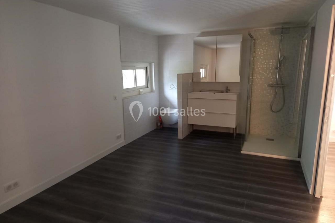 Chambre avec sol en parquet sombre, salle d'eau intégrée comprenant douche, lavabo et toilettes, éclairée par une fenêtre.