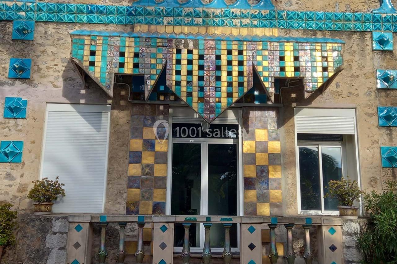 Façade ornée de mosaïques colorées avec motifs géométriques, encadrant une fenêtre et une petite terrasse.