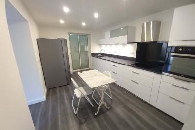 Salle lumineuse avec une grande table dressée pour un repas, décorée de fleurs blanches et rouges, entourée de chaises…