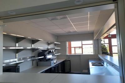 Miniature Bar Accueil lumineux avec comptoir blanc, porte vitrée à gauche laissant entrer la lumière et plante verte à droite.