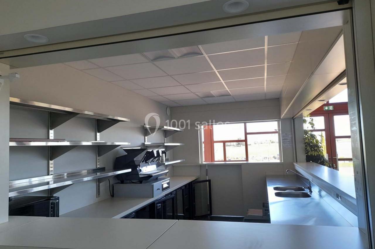 Cuisine professionnelle moderne avec plans de travail en inox, étagères murales et grandes fenêtres laissant entrer la…