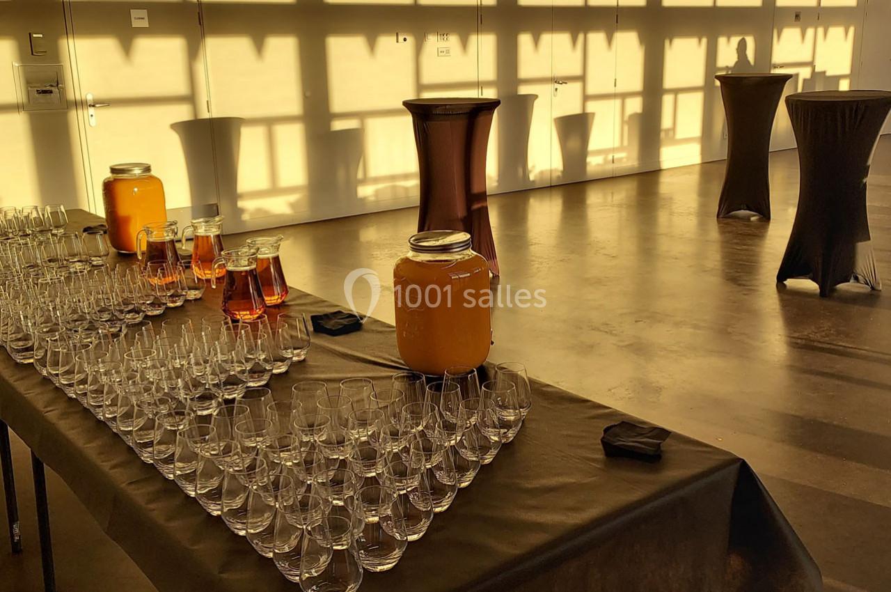 Table dressée avec des verres, carafes de jus et nappes noires dans une salle baignée de lumière dorée.