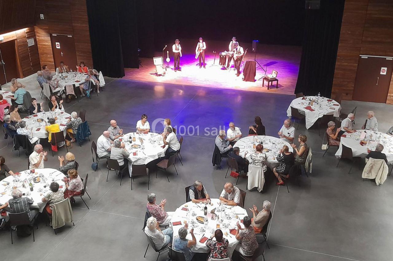 Des personnes assises autour de tables rondes dans une salle, assistent à une performance musicale sur scène.